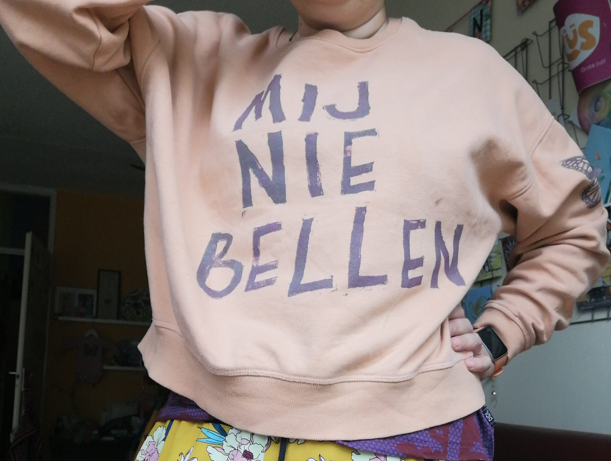 Bovenlijf vlak voor de camera met een perzikkleurige trui. Erop staat gedrukt: mij niet bellen