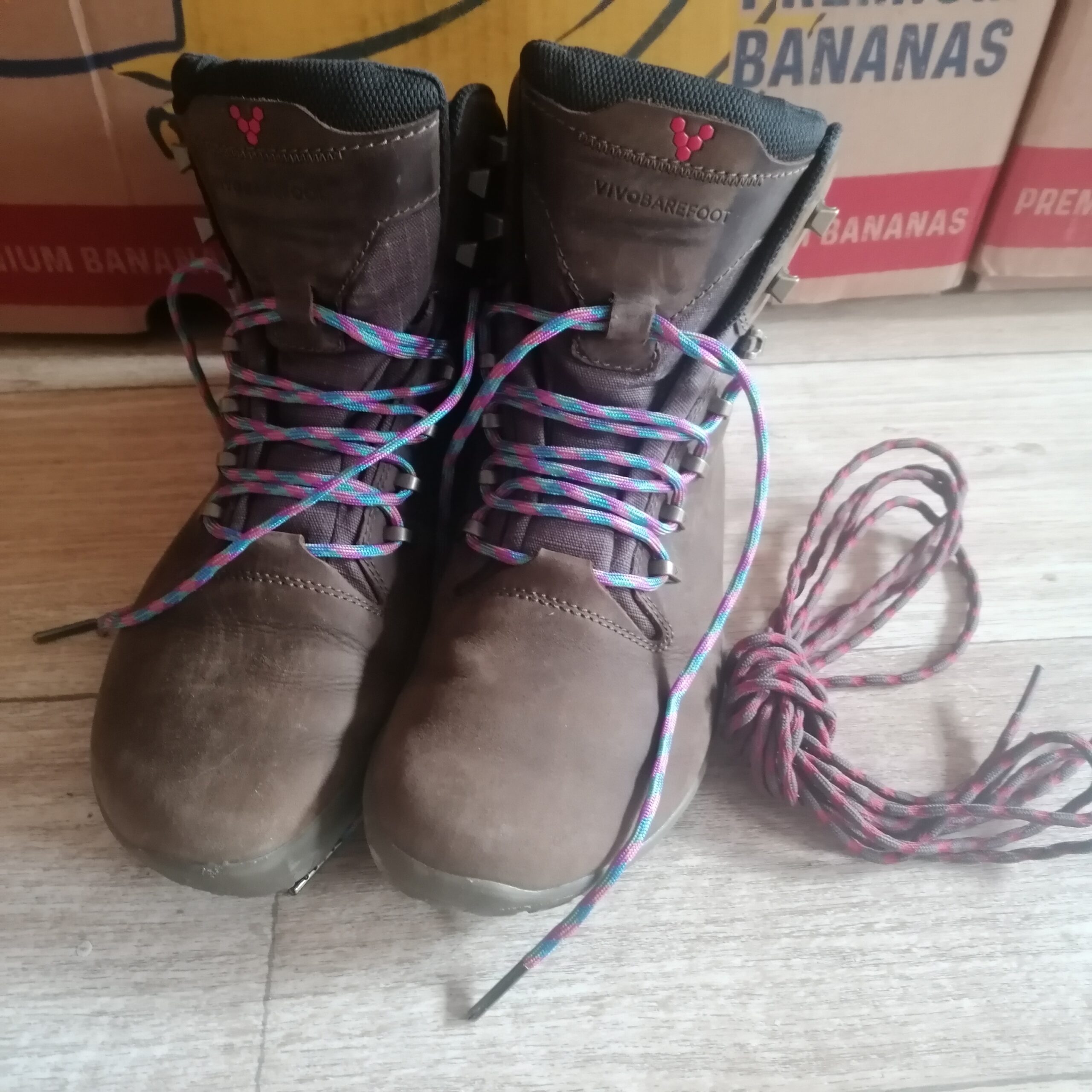 Paar donkerbruine wandelschoenen met gekleurde veters erin. Ernaast ligt nog een paar veters.